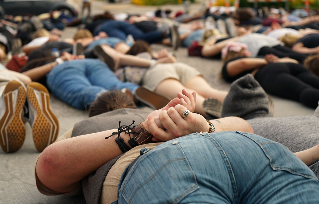 Protesting crowd lay on the ground with their hands behind their backs in a handcuffed pose